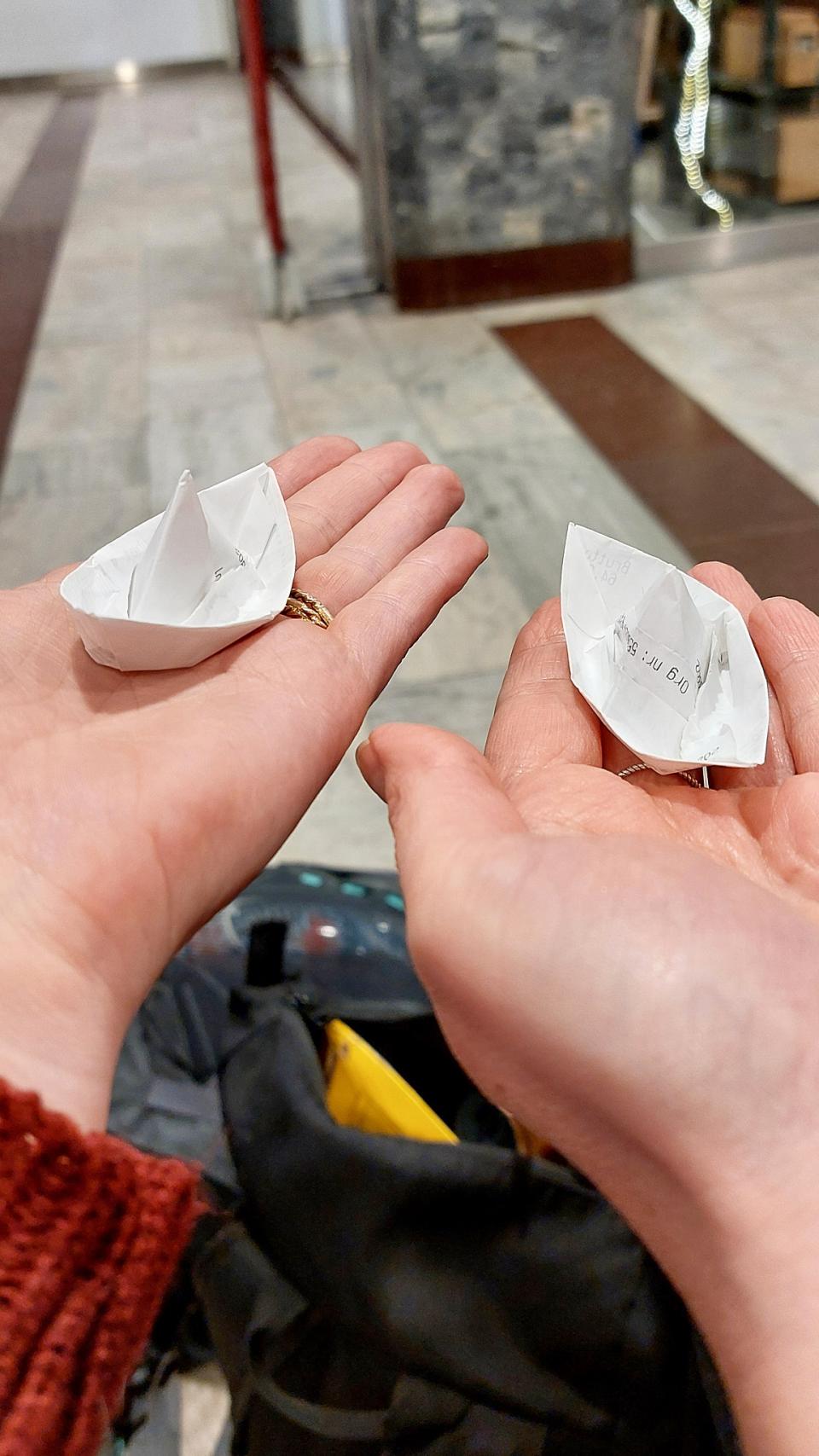 Kaksi pienikokoista paperilaivaa kahdella kämmenellä.